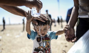 Κούρδος από τη Συρία δροσίζει τον μικρό πρόσφυγα που μόλις πέρασε τα σύνορα Συρίας – Τουρκίας, κοντά στη πόλη Suruc στην επαρχία Sanliurfa  της ΝΑ Τουρκίας. 20 Σεπτέμβρη 2014