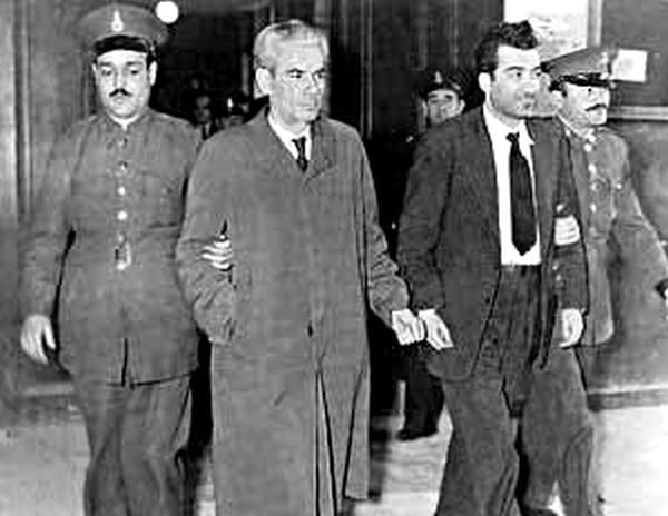 O Νίκος Μπελογιάννης δεμένος με χειροπέδες οδηγείται στο δικαστήριο μαζί με ένα από τα παλιότερα στελέχη του ΚΚΕ, Στέλιο Γραμμένο. Όσοι πήγαιναν στα γραφεία της ΚΟΑ μετά τη μεταπολίτευση το 1974 θυμούνται με συγκίνηση τον μπαρμπά – Στέλιο Γραμμένο.