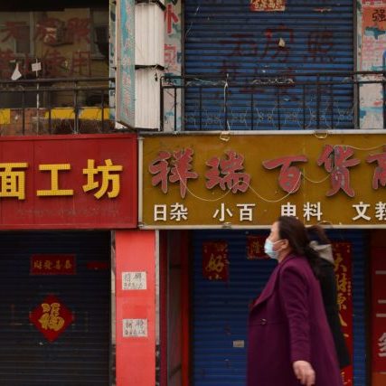 Women wearing face masks walk past closed shops in Suifenhe