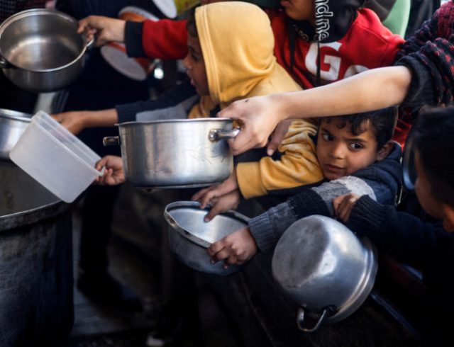 Palestinian children wait to receive food cooked by a charity kitchen amid shortages of food supplies, in Rafah