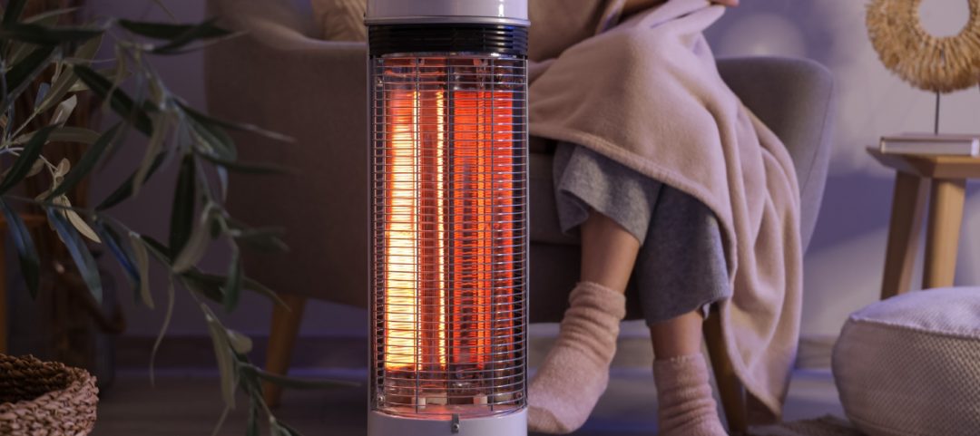 Young,Woman,With,Electric,Heater,And,Blanket,Sitting,On,Armchair