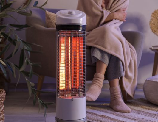 Young,Woman,With,Electric,Heater,And,Blanket,Sitting,On,Armchair