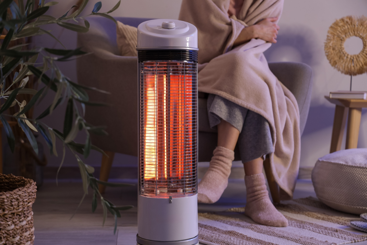 Young,Woman,With,Electric,Heater,And,Blanket,Sitting,On,Armchair